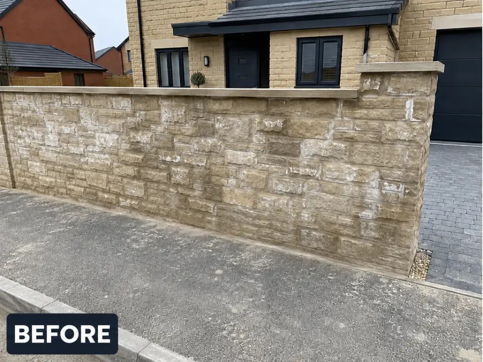 Stone boundary wall dulled by cement haze, algae and construction soiling before cleaning